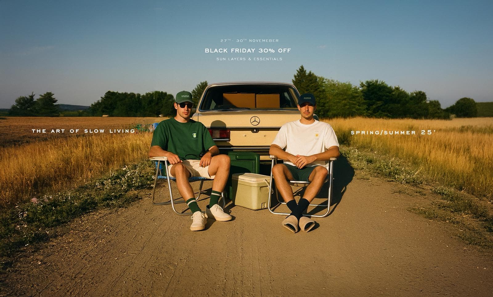 Two friends in Common C tees and caps resting on camping chairs behind a vintage car